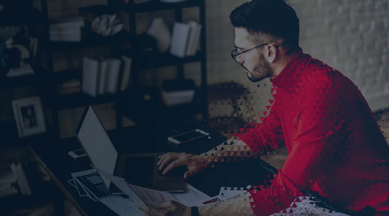 Pensive bearded young man in eyeglasses checking information on website on modern laptop computer using wireless internet.Concentrated graphic designer with sketches in hands working on freelance