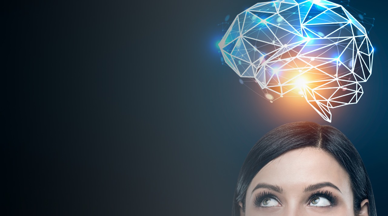 Close up of a black haired woman s head looking to the left and standing near a dark blue wall with a blue brain hologram shining with an orange light above her head